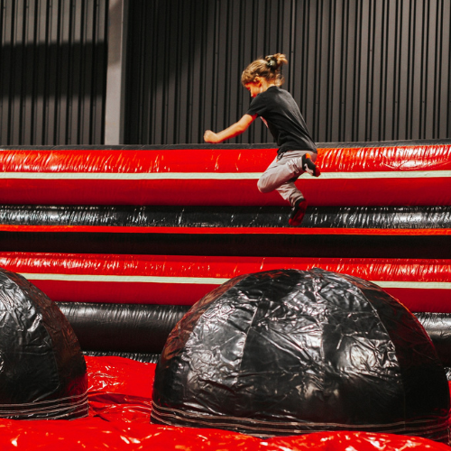 Une petite fille qui saute sur un parcours de wipe out dans une structure gonflable rouge et noir au Ninja Factory sur la rive-sud de montréal. 